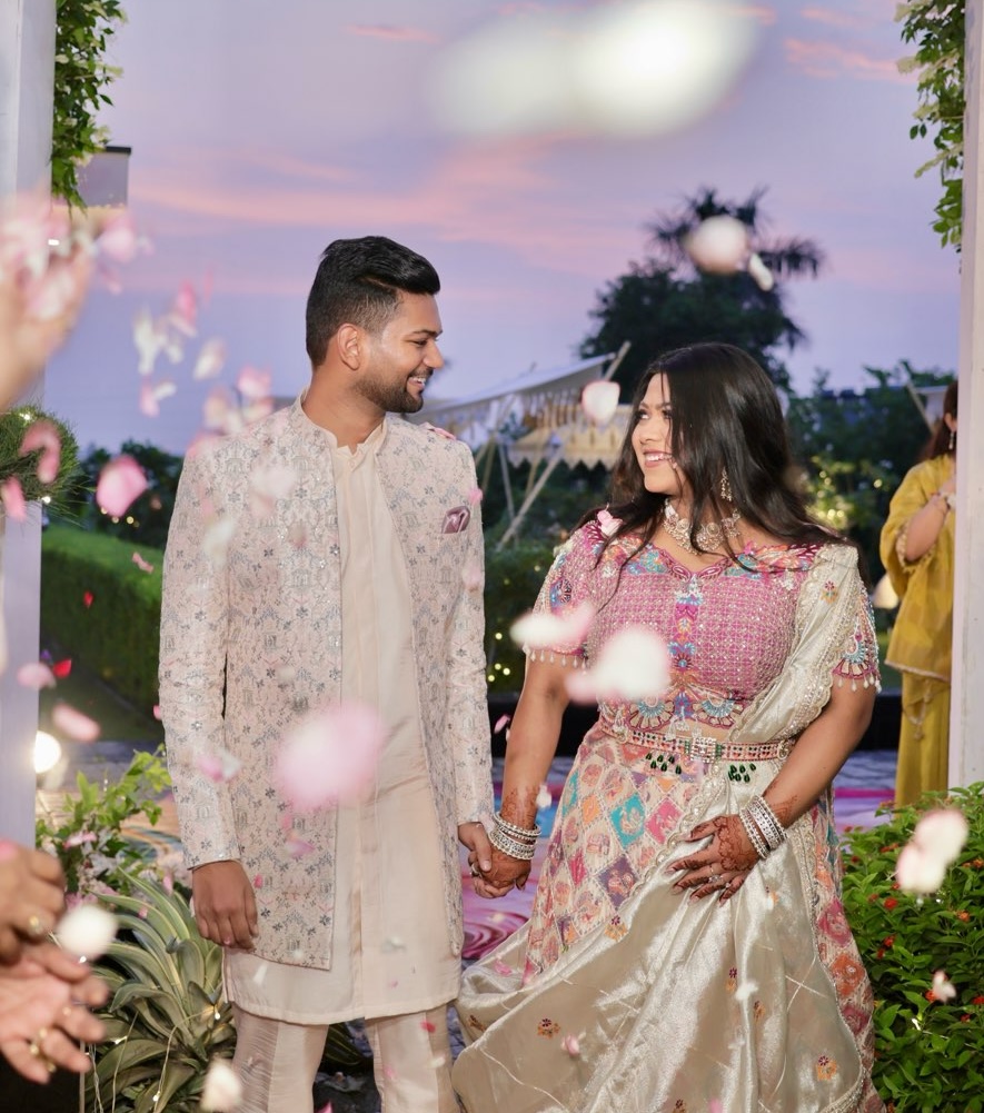 Aakanksha and Lovekesh, laughing, in a shower of petals at dusk